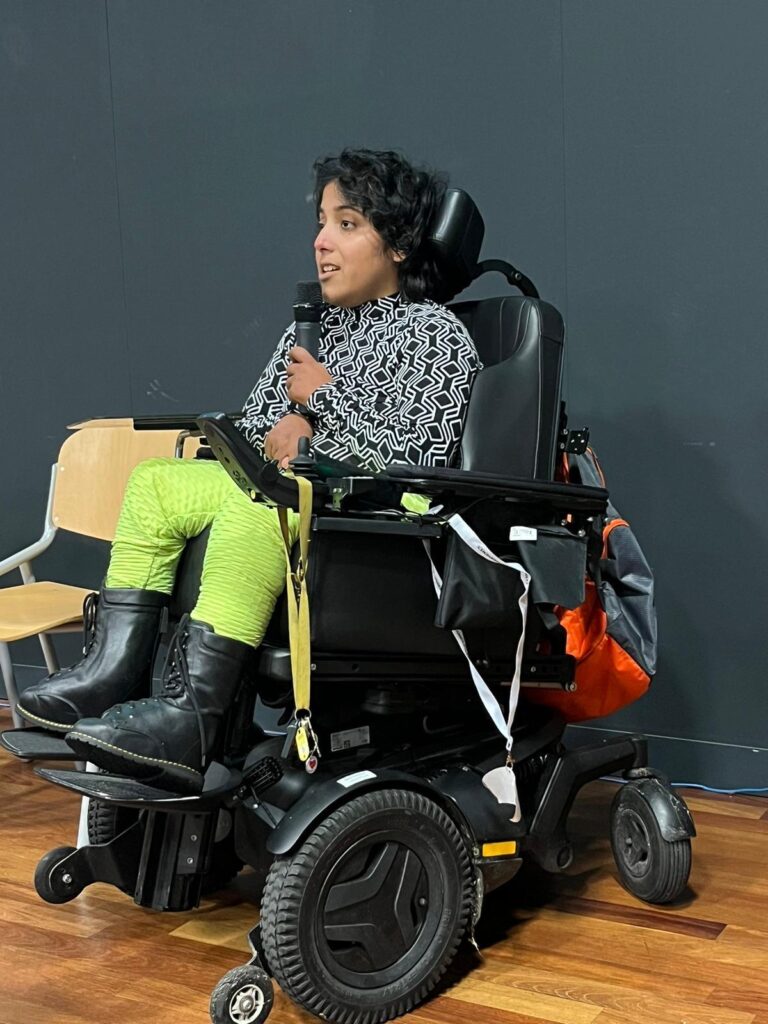 Dailisha spreekt met een microfoon vanuit haar elektrische rolstoel